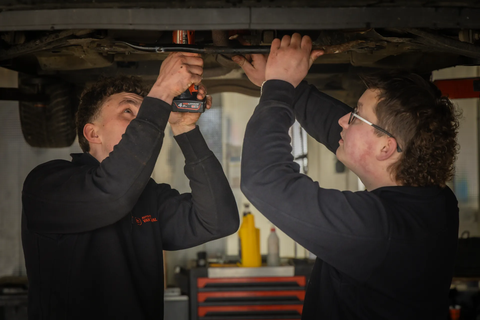 Twee monteurs werken samen onder een auto op de brug in de werkplaats