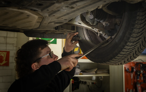 Seth inspecteert wielophanging onder een auto tijdens APK keuring